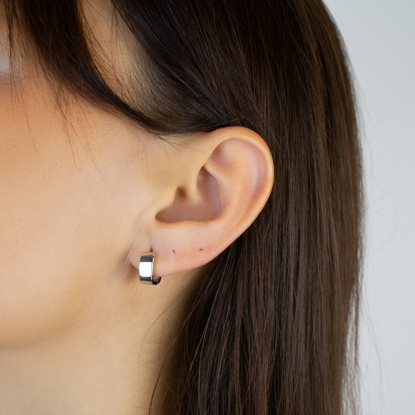 Cercei argint placat cu rodiu cu design patratos la urechea unei femei Montana close up on a women wearing sterling silver rhodium plated square design hoop earrings