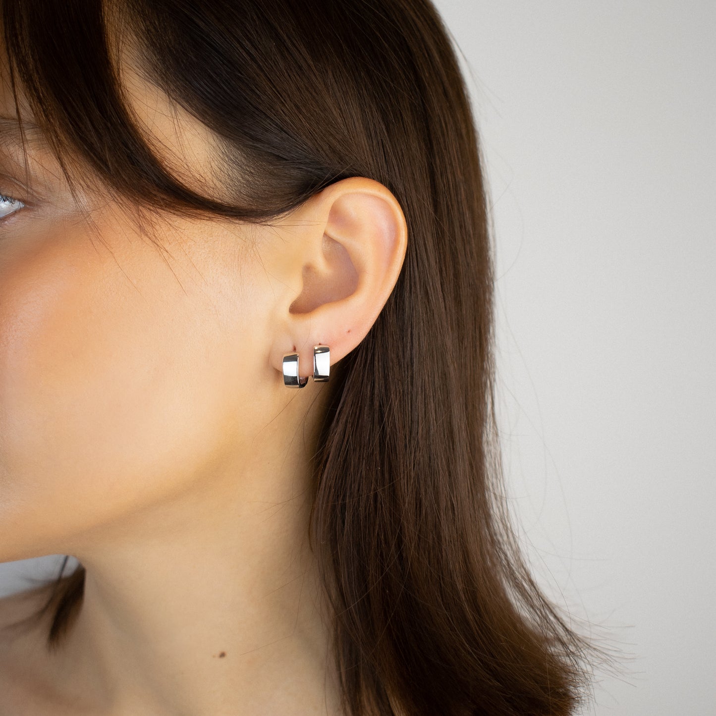 Cercei argint placat cu rodiu cu design patratos la urechea unei femei Montana close up on a women wearing sterling silver rhodium plated square design hoop earrings