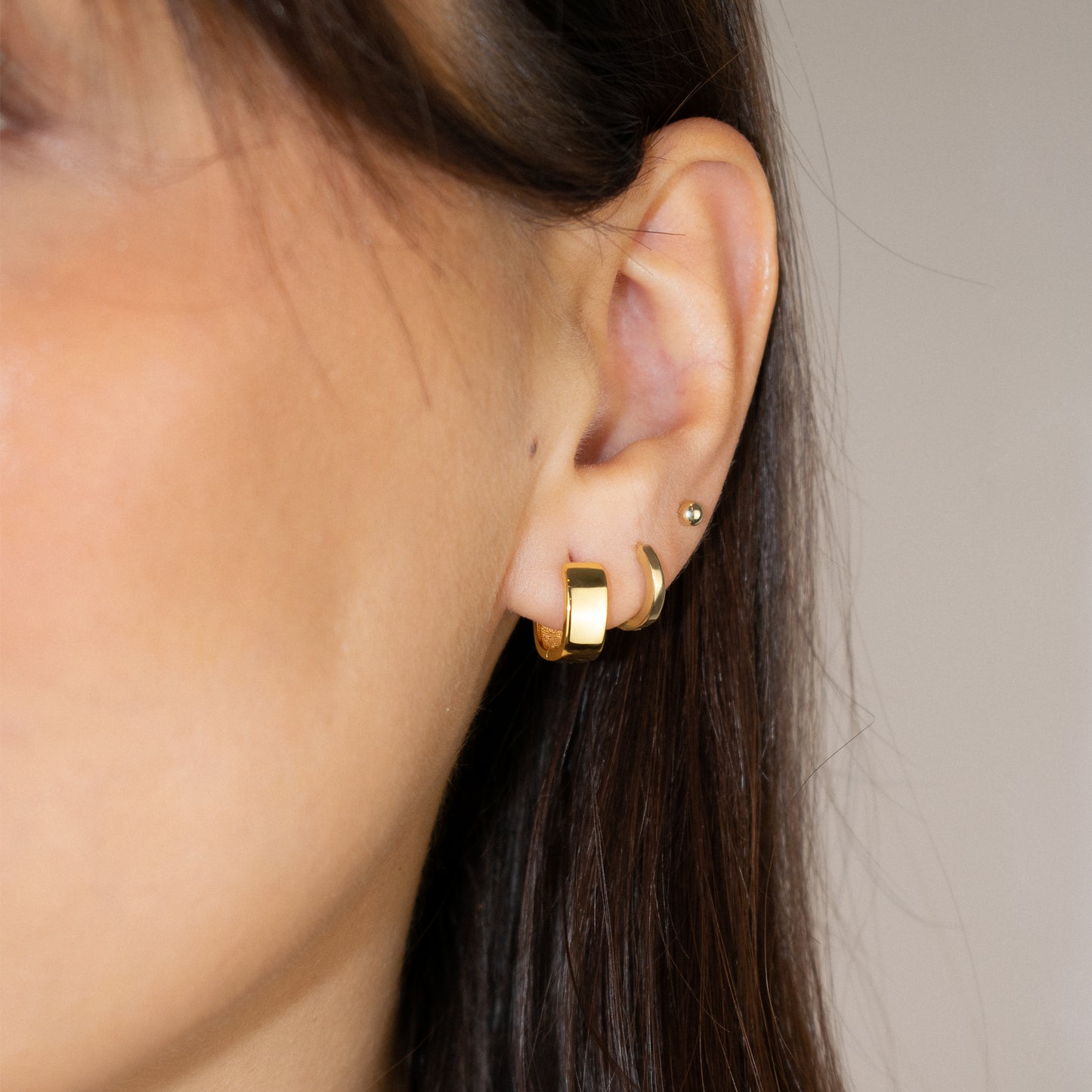 Cercei argint placat cu aur 18K cu design patratos la urechea unei femei Callie close up on a woman wearing a gold vermeil square design hoop earrings