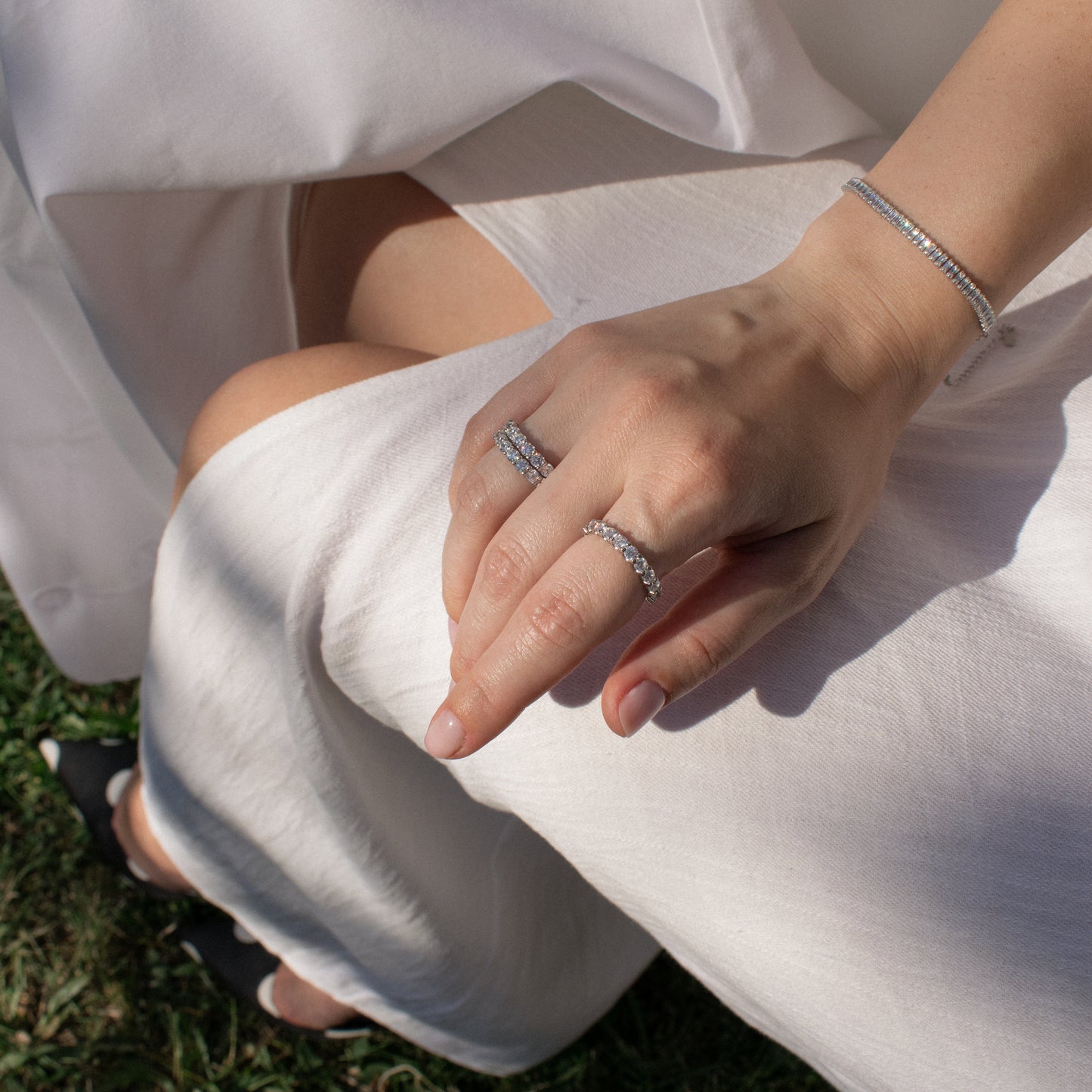A close-up of a person's hand resting on their lap, wearing two silver rings and a matching silver bracelet with emerlad cut zirconia stones.