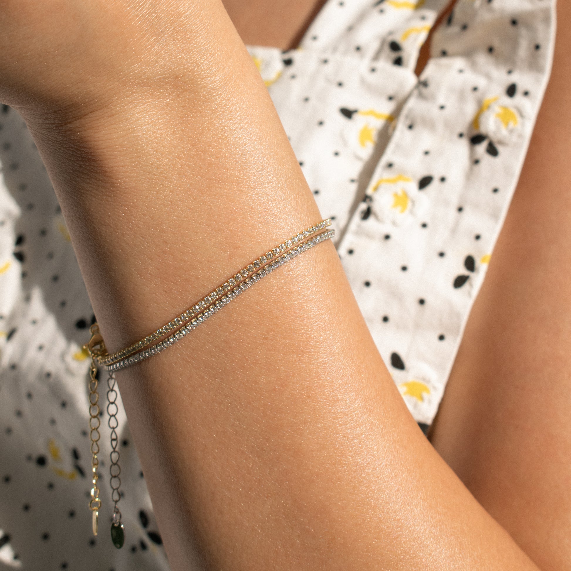 A close-up of two sterling silver tennis bracelets with zirconia stones one silver and one gold plated worn on a woman's wrist. 