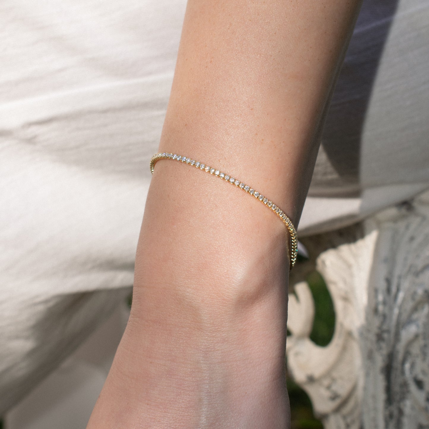 A delicate sterling silver gold plated tennis bracelet with zirconia stones, worn on a person's wrist against a soft white background.