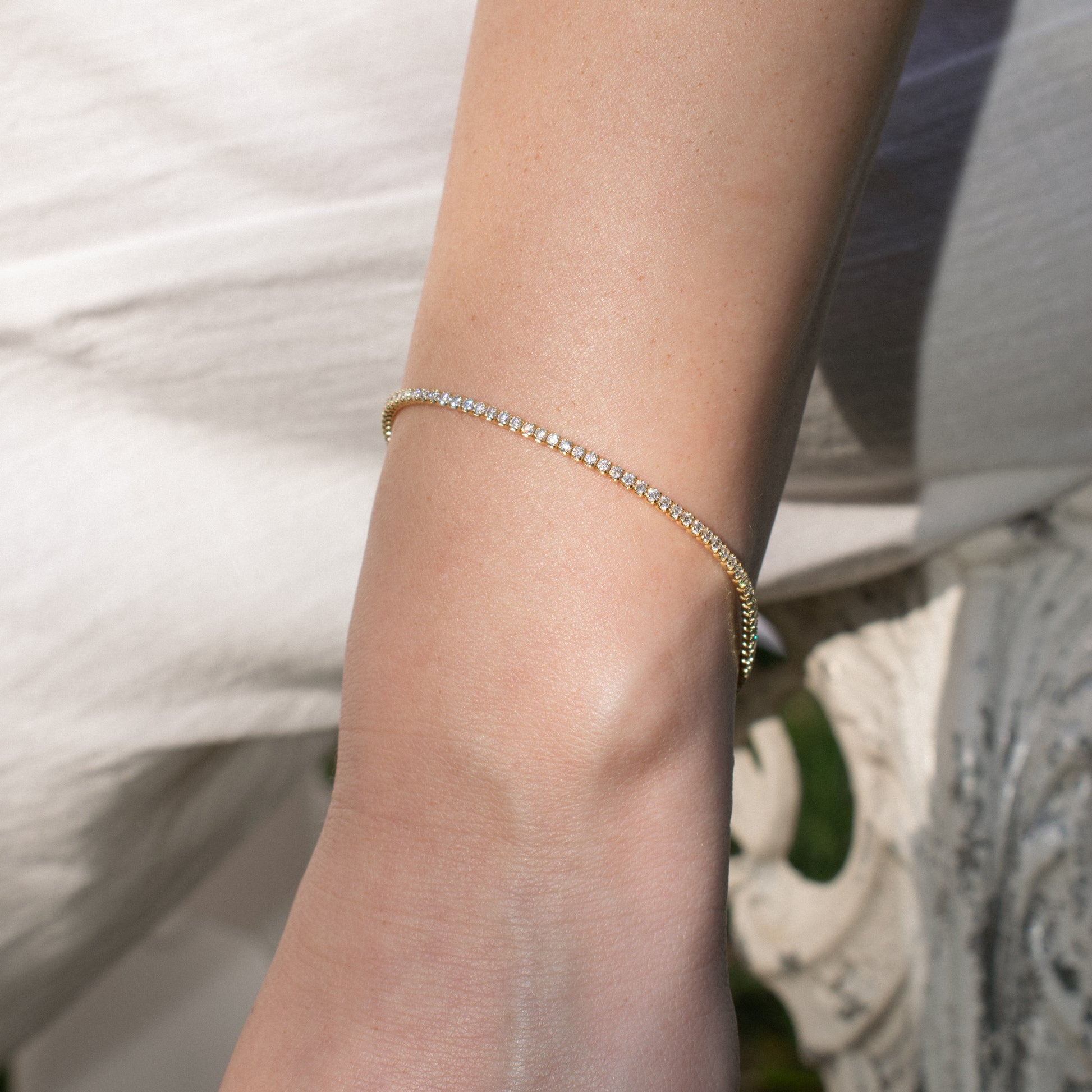 A delicate sterling silver gold plated tennis bracelet with zirconia stones, worn on a person's wrist against a soft white background.