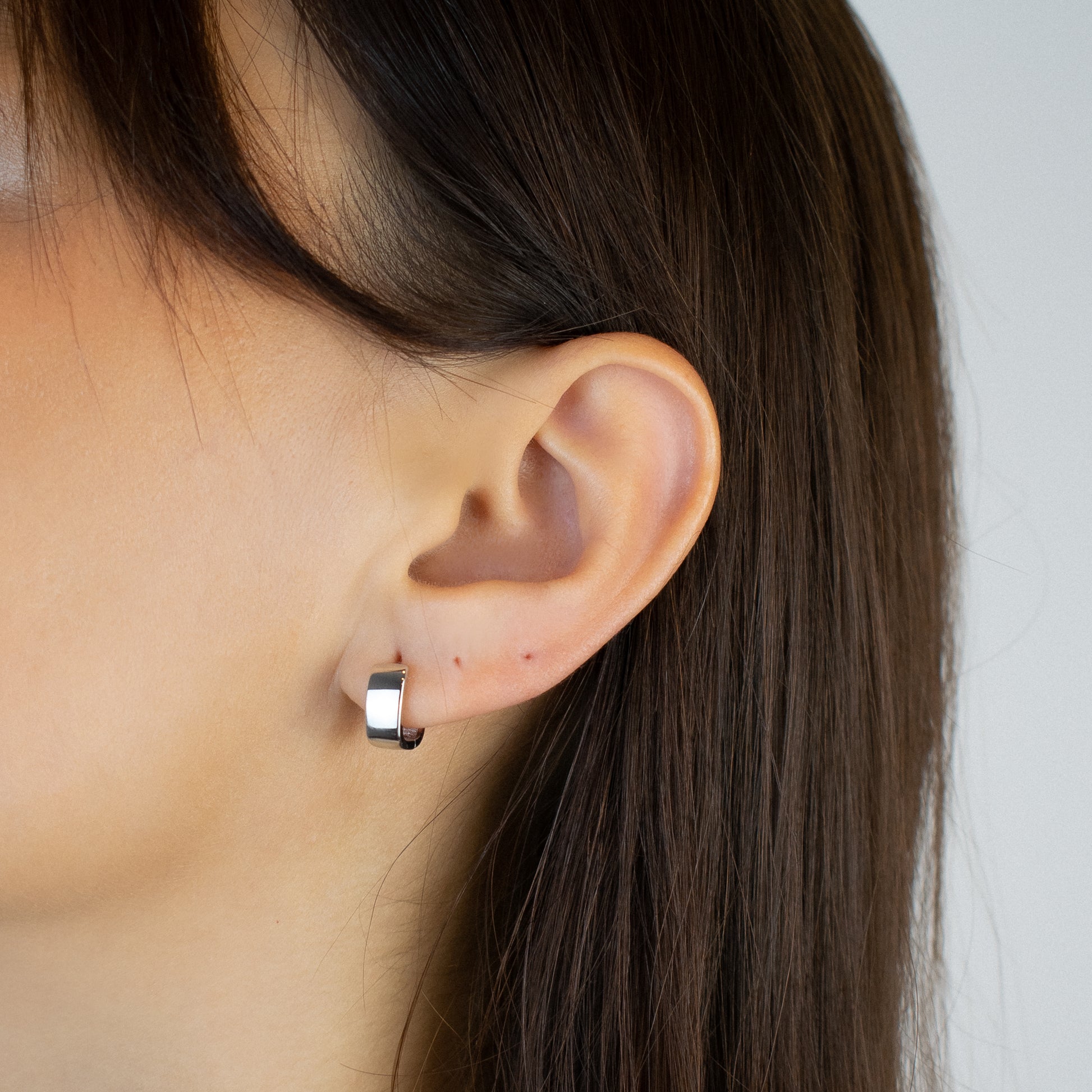 Cercei argint placat cu rodiu cu design patratos la urechea unei femei Montana close up on a women wearing sterling silver rhodium plated square design hoop earrings 