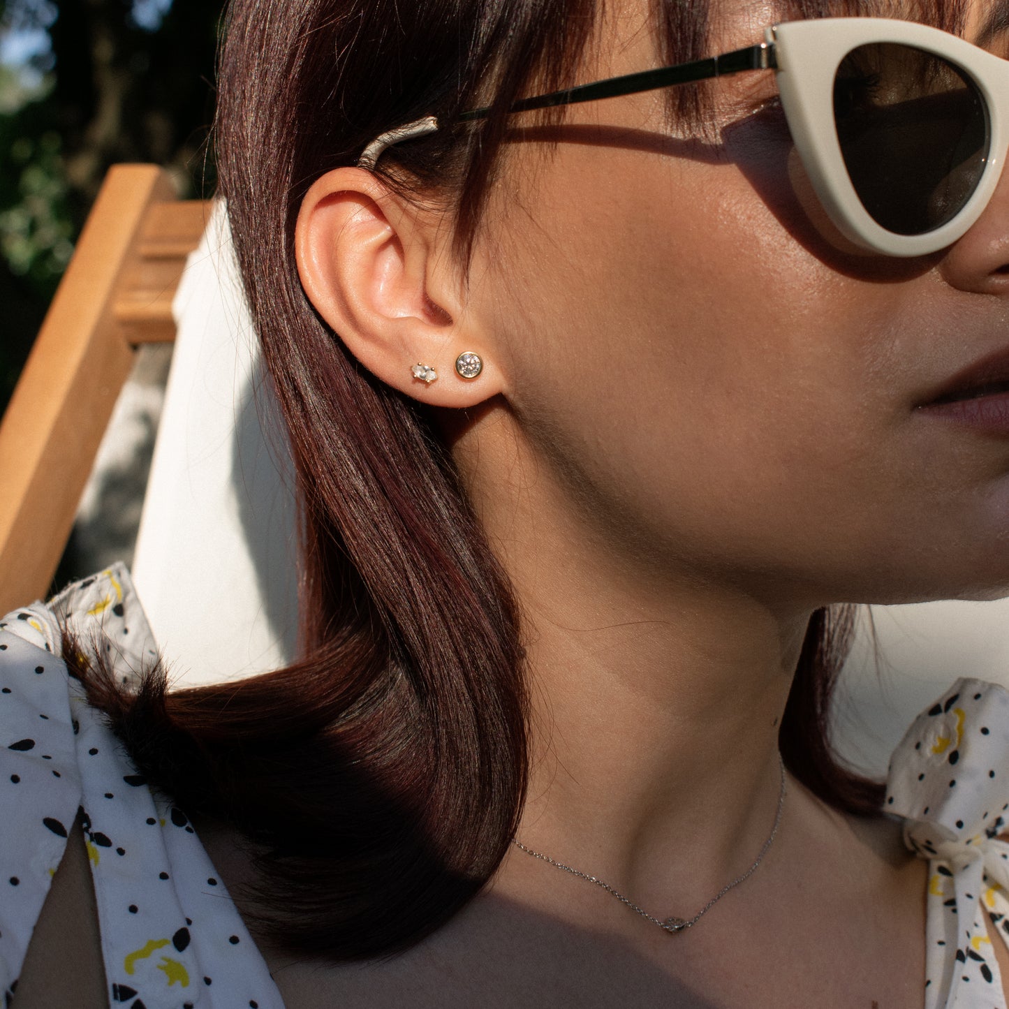 Close-up of a person's ear wearing two small stud earrings: one piercing silver with a clear Marquise stone and a flat back  and one gold with circular moissanite stone.