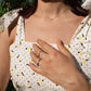 A close-up lifestyle shot of a woman wearing delicate tiny pave silver necklace with zirconia stones paired  silver rings, including a thin band ring and a ring with a small clear gemstone.