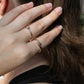 A close-up of a person's hand wearing two slim silver rings, one with a small round clear gemstone and one open-ended band, against dark brown hair.