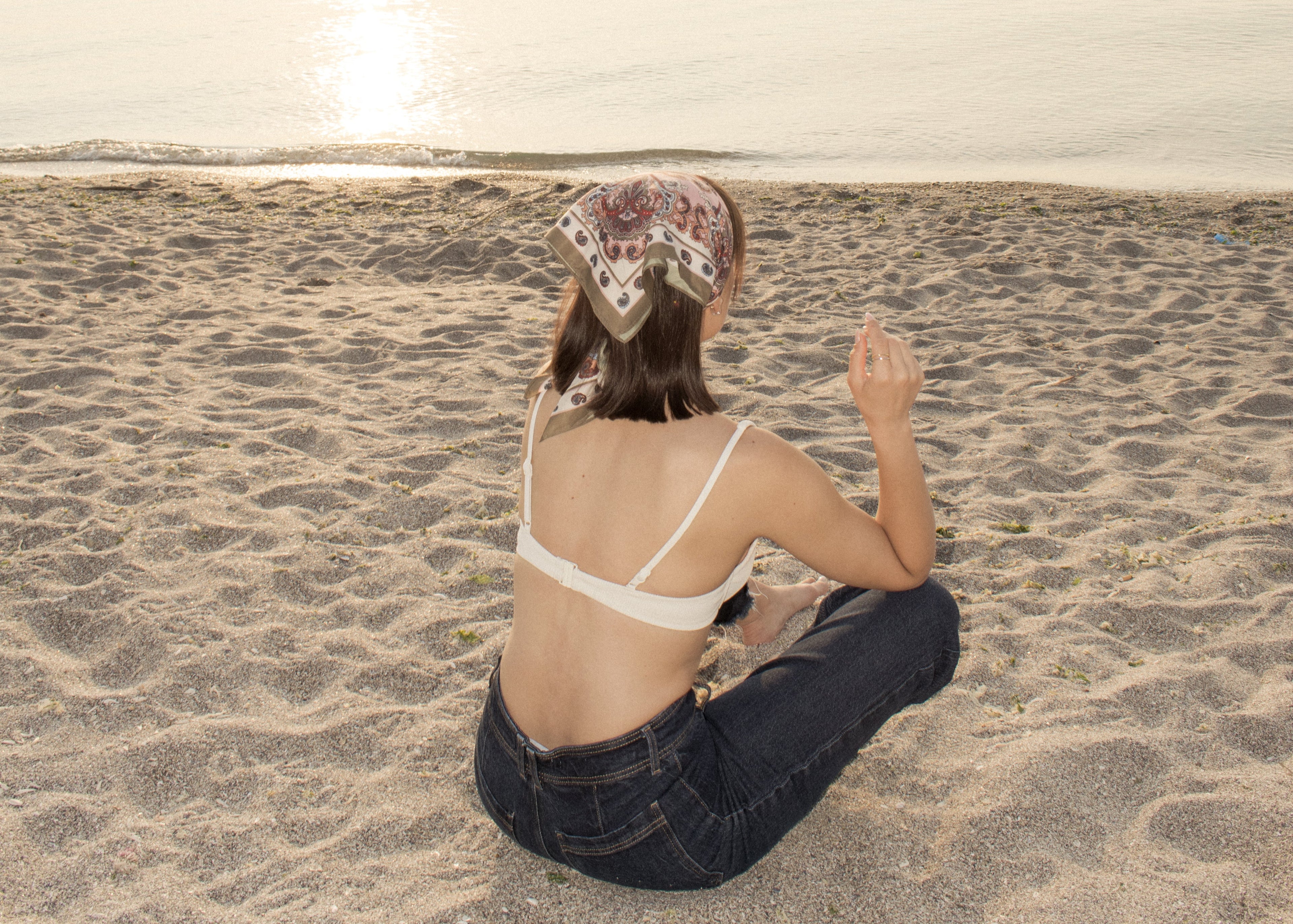 Femeie stand pe nisip care poarta doua inele de argint, unul placat cu rodiu, altul placat cu aur 18k vermeil privind marea. Woman sitting on a sandy beach with sterling silver rings on her finger, one rhodium plated and one 18k gold vermeil,  facing the ocean.