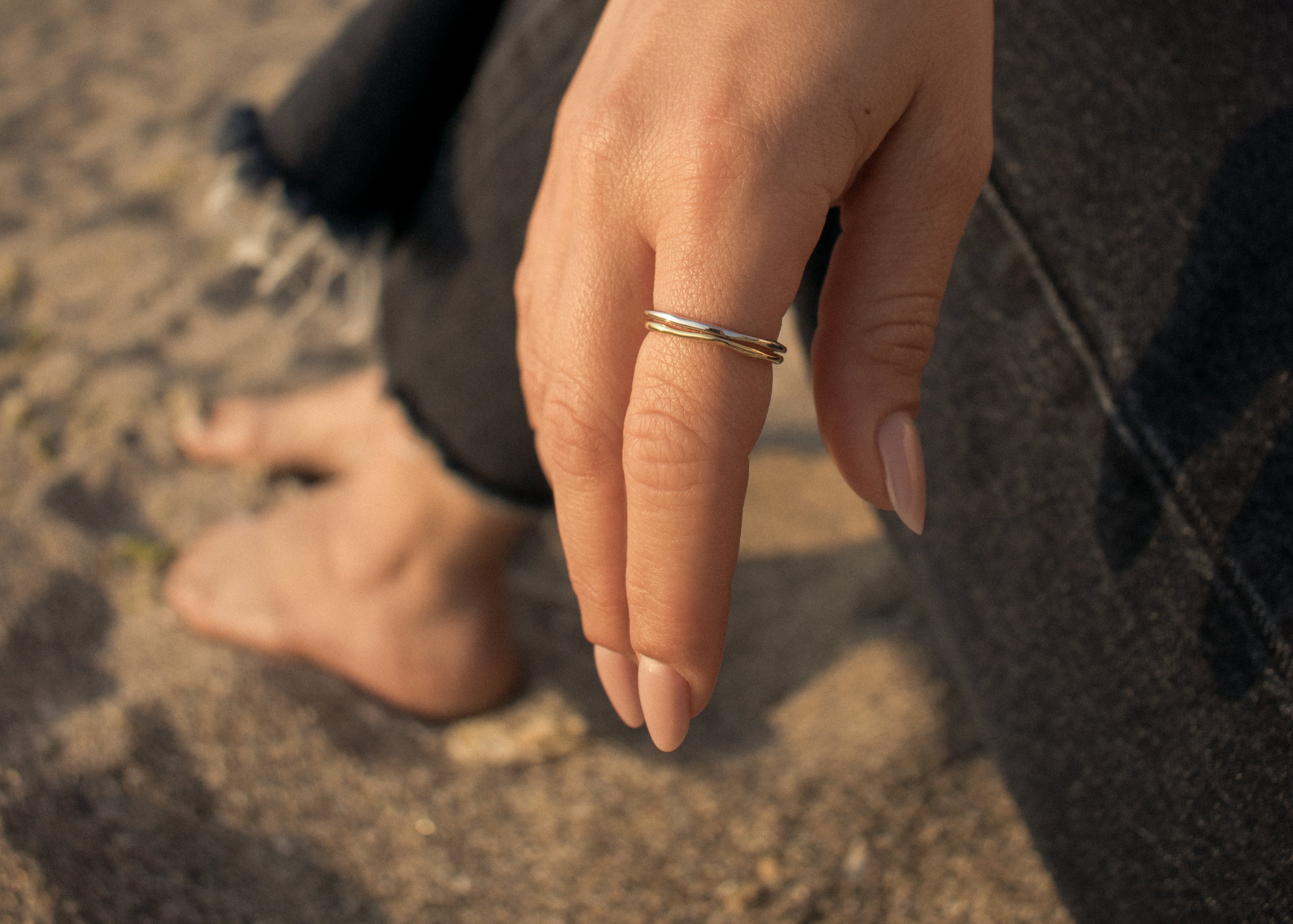 Mana a unei femei care poarta doua inele de argint, unul placat cu rodiu, iar celalalt placat cu aur 18k vermeil pe o plaja. Hand with a sterling silver ring and a 18k gold vermeil ring on a beach